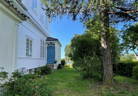 Hvitt trehus med blå inngangsdør og grønn hage rundt