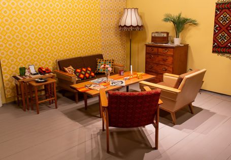 Salong med en liten sofa, to stoler, et sofabord, settebord, lampe og kommodeseksjon. Pyntegjenstander på bordene.