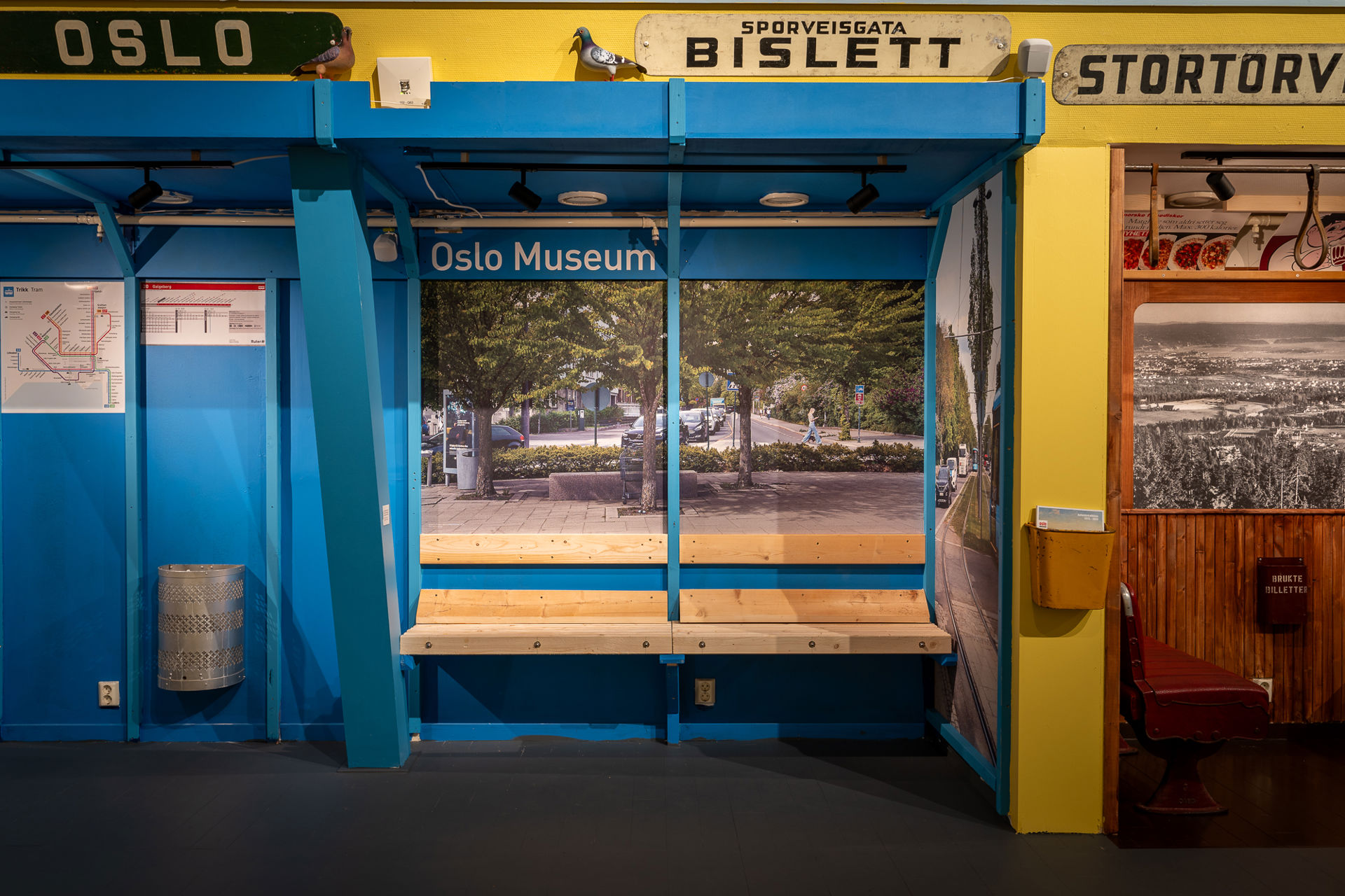 Replika av et nytt blåmalt trikkestopp med trebenker og teksten Oslo Museum over stoppet, som del av en utstilling.