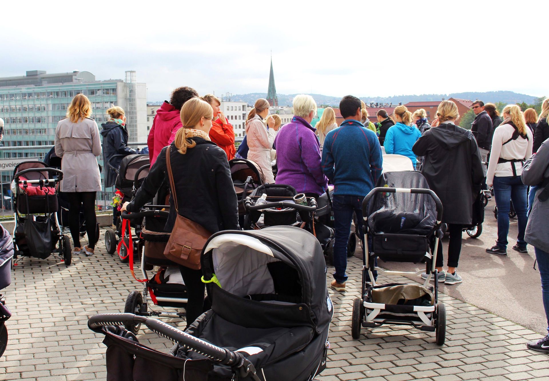 Personer med barnevogn utendørs i Oslo sentrum med ryggen til