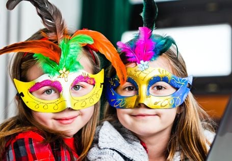 To smilende jenter med fargerike masker med fjær