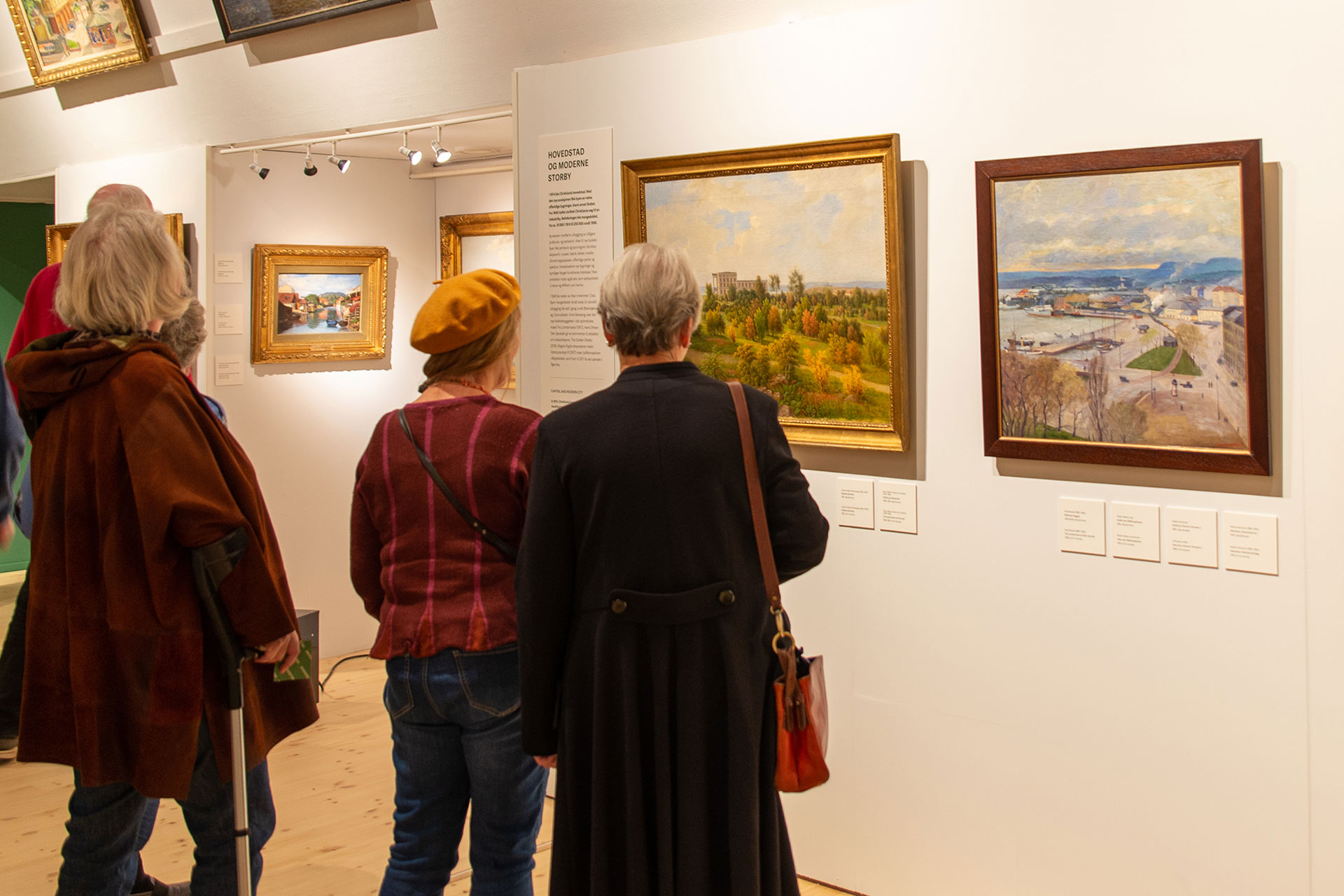 Fire mennesker står og ser på malerier av Oslo fra gamle dager.