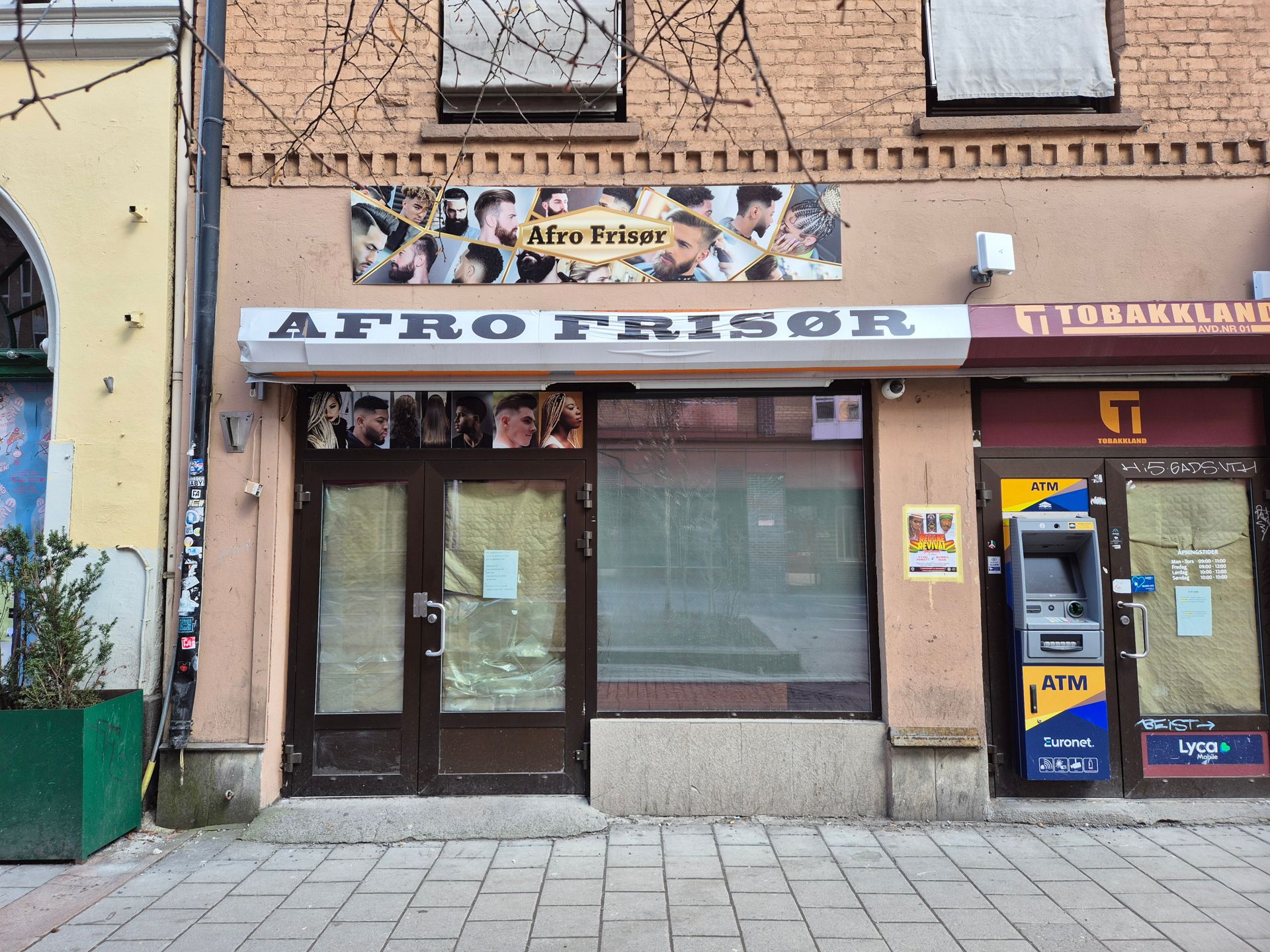 Fasade på bygg med vinduer og dører dekket av papp. Skilt med Afro Frisør.